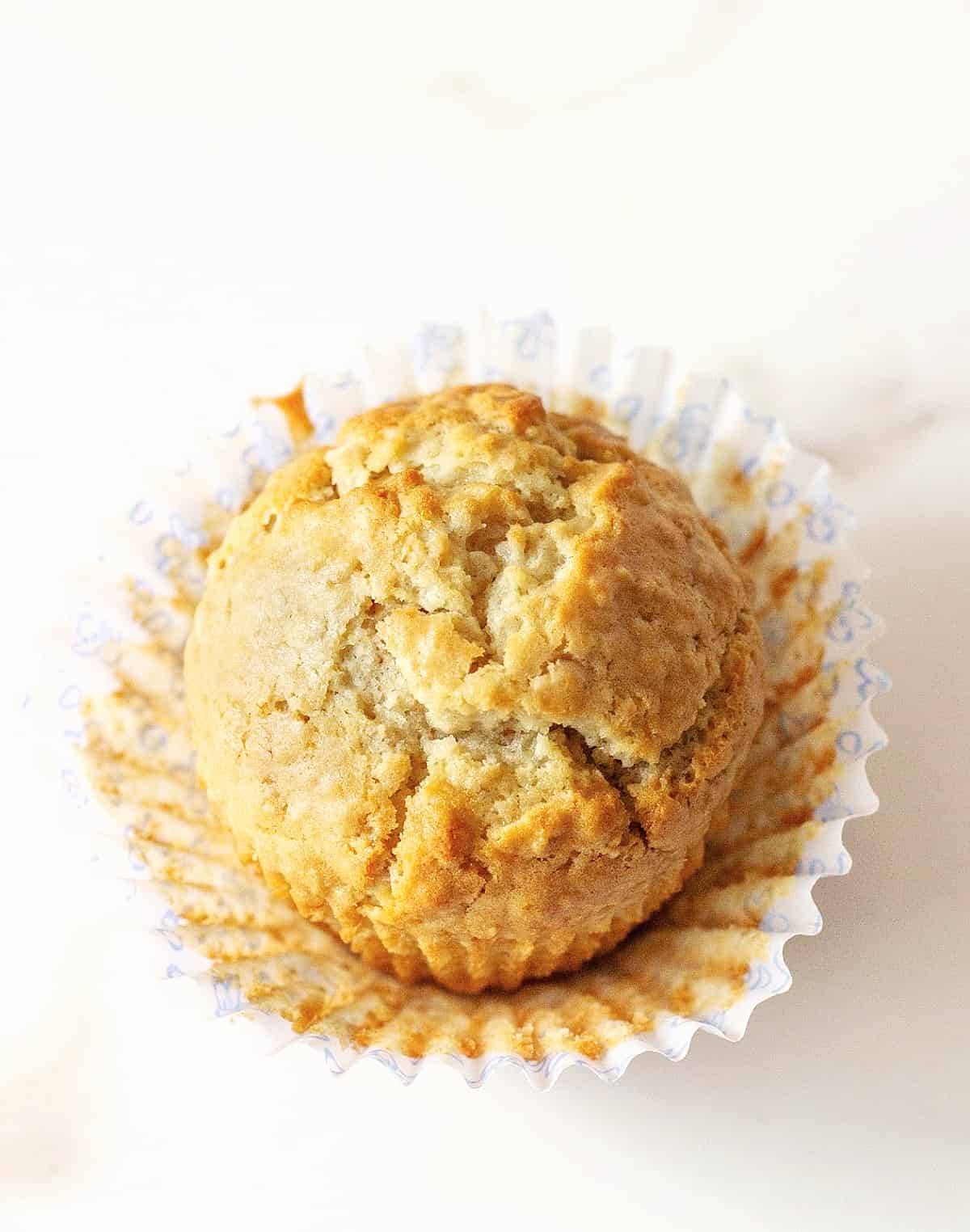 One golden colored muffin on an opened whitish paper cup, white surface.