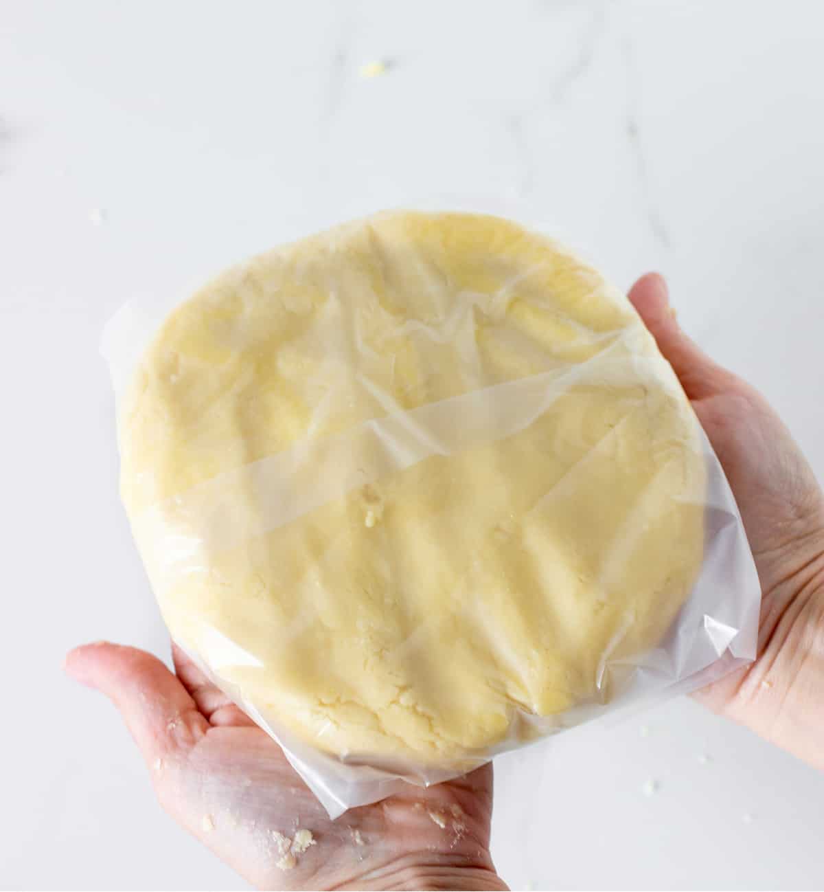 Two hands holding wrapped disc of dough