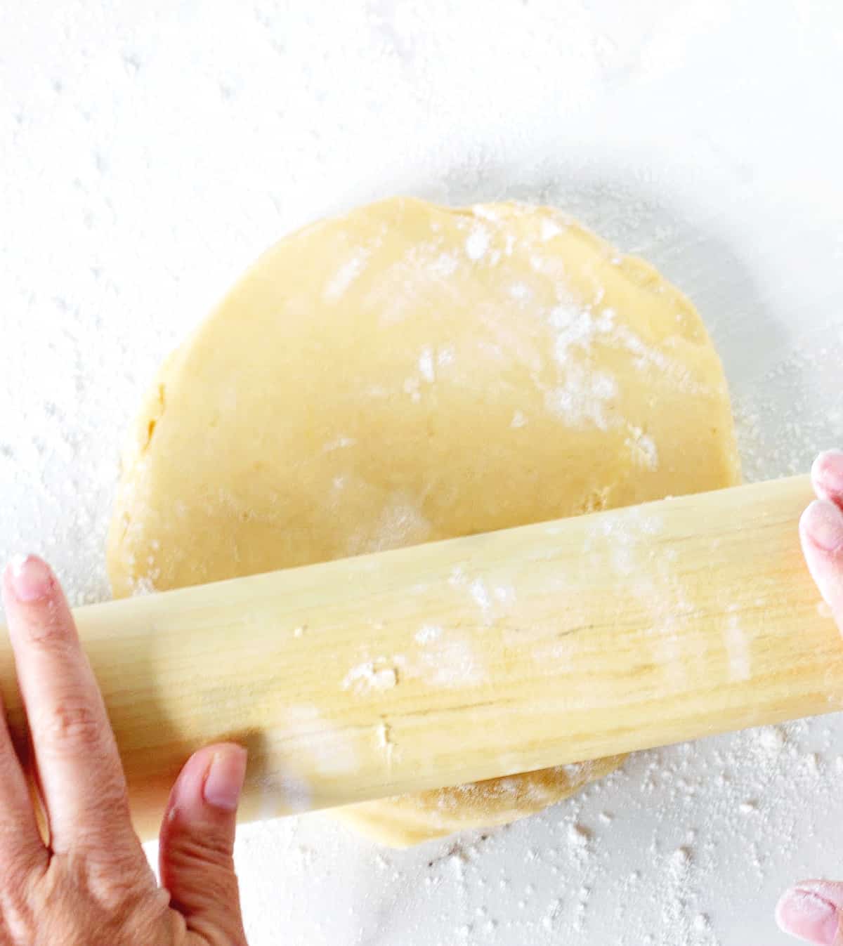 Hands rolling disc of dough with pin on white surface