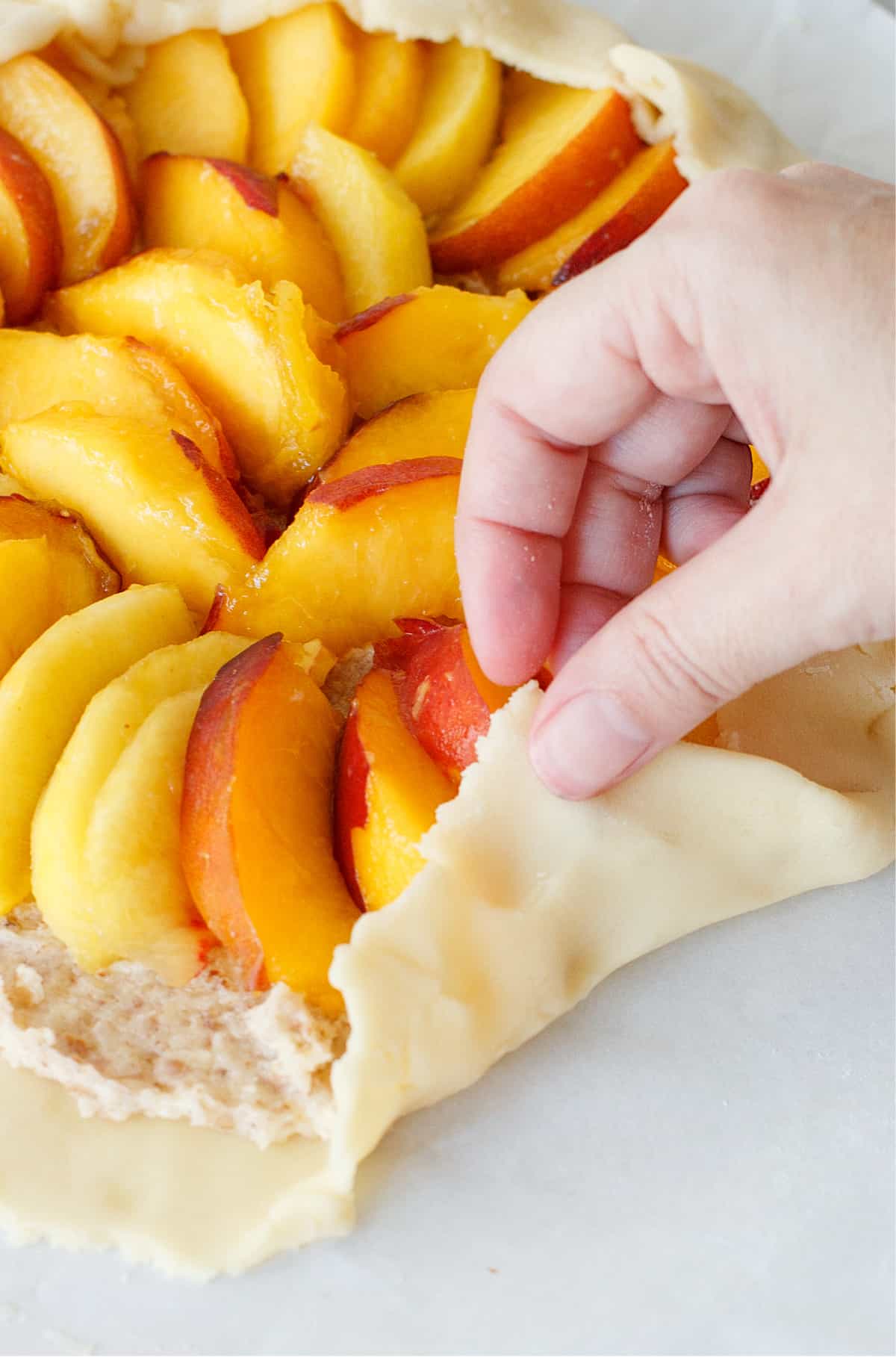 Hand folding edges of pie crust inwards. Sliced peaches inside.