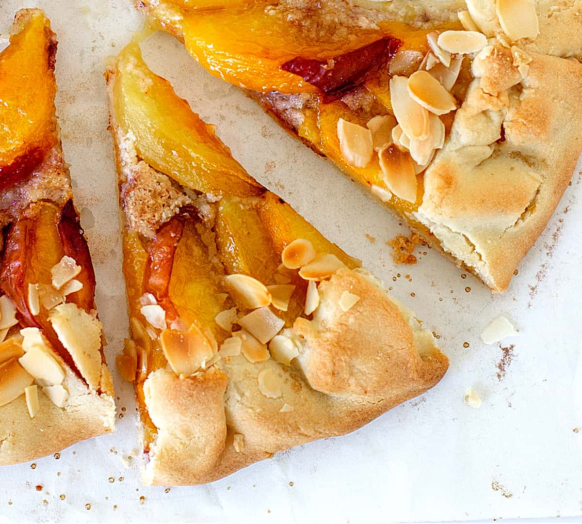 Close-up of two slices of baked peach galette on a white surface.