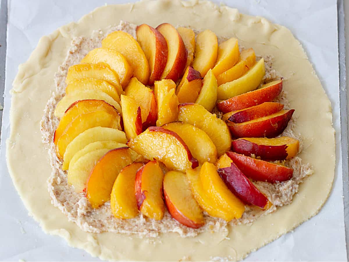 Round of pie dough on metal baking sheet with circle of peach slices and almond cream.