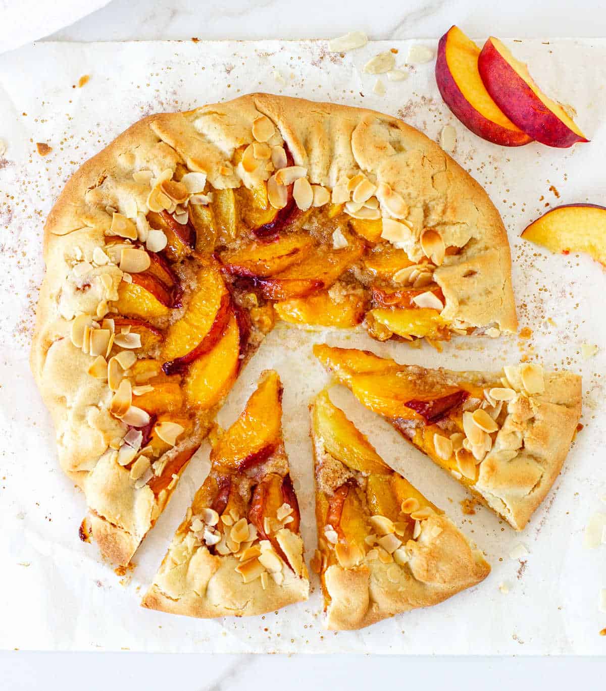 Whole baked peach galette on parchment paper, top view.