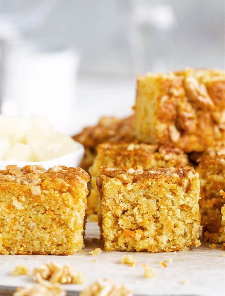 Stacked squares of carrot cake with walnuts, grey and white background