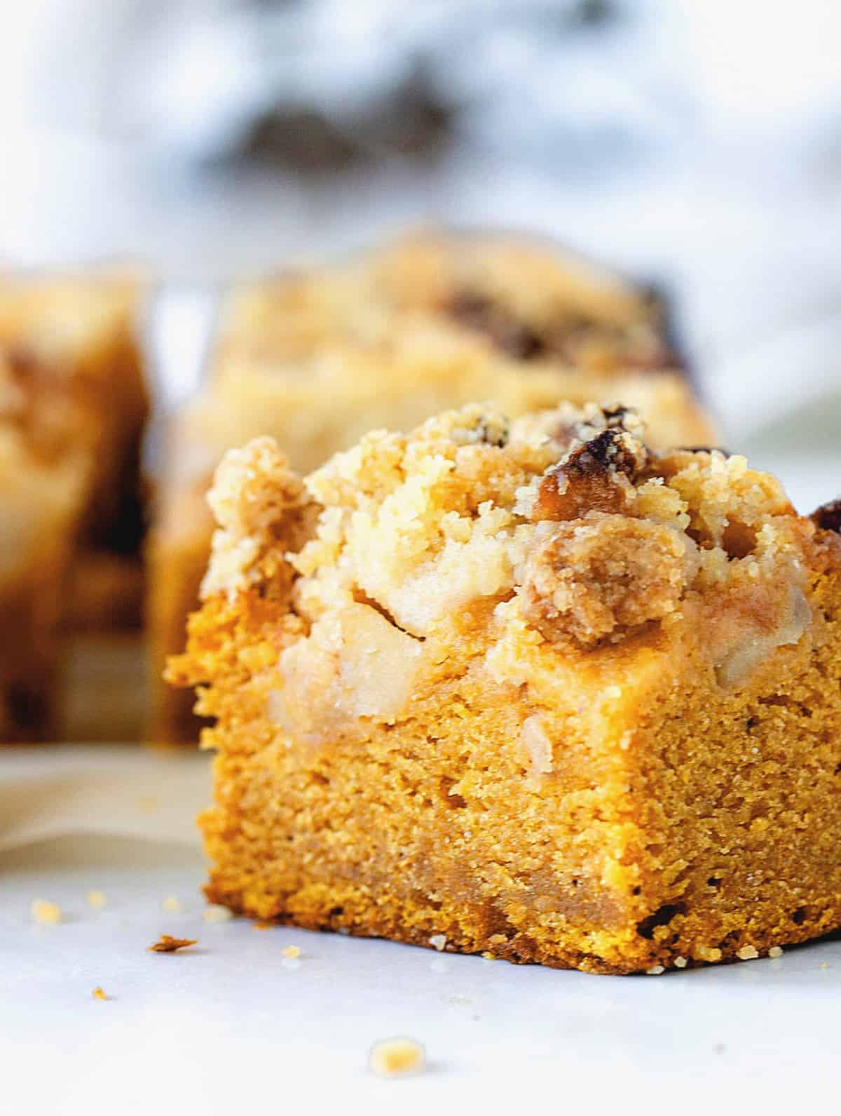 Close-up of pumpkin crumble cake square, white surface, greyish background
