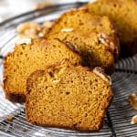 A wire rack with slices of pumpkin walnut bread on a white surface.