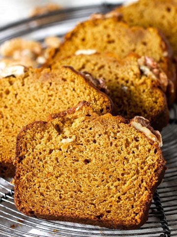 A wire rack with slices of pumpkin walnut bread on a white surface.