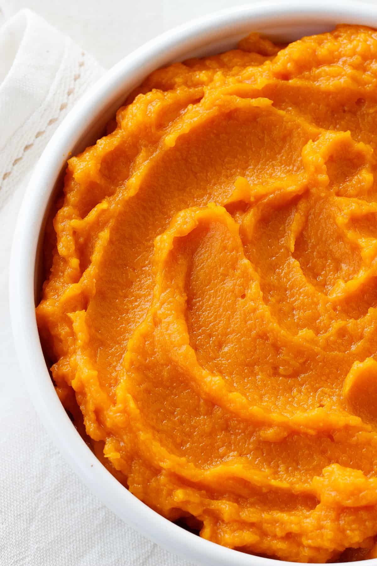 Partial view of pumpkin puree in white bowl on white surface