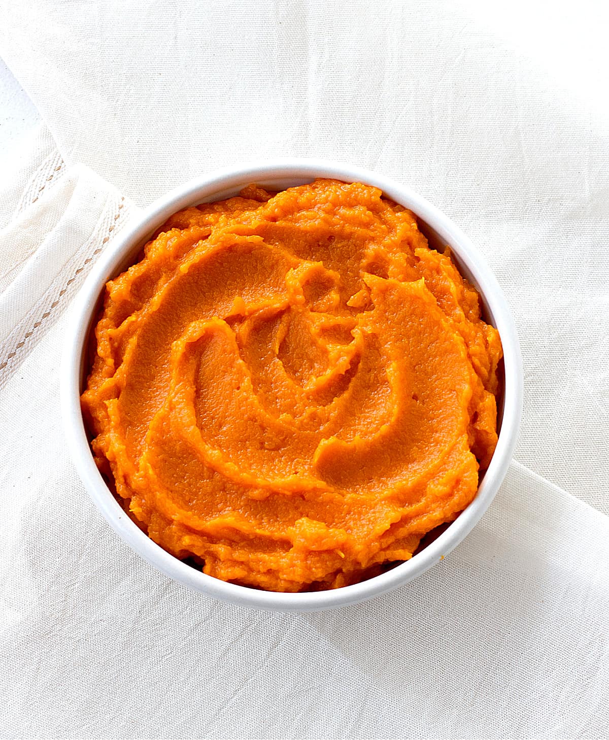 On a whitish piece of linen, a white bowl filled with pumpkin puree.