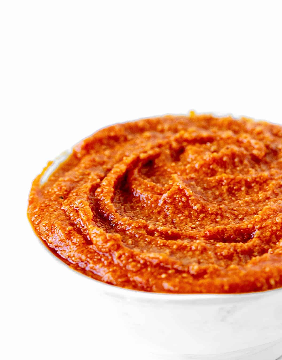 Orange red rustic sauce in white bowl on a very white background.