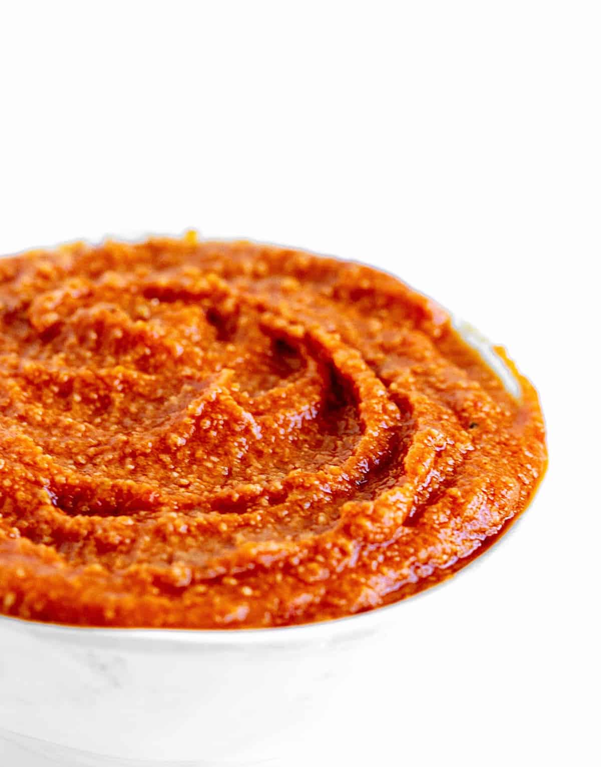 Reddish orange salsa romesco in a white bowl, white background