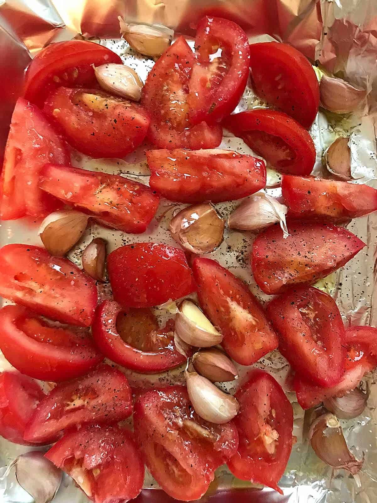 Pieces of tomatoes, red peppers, and garlic cloves on aluminum paper. 