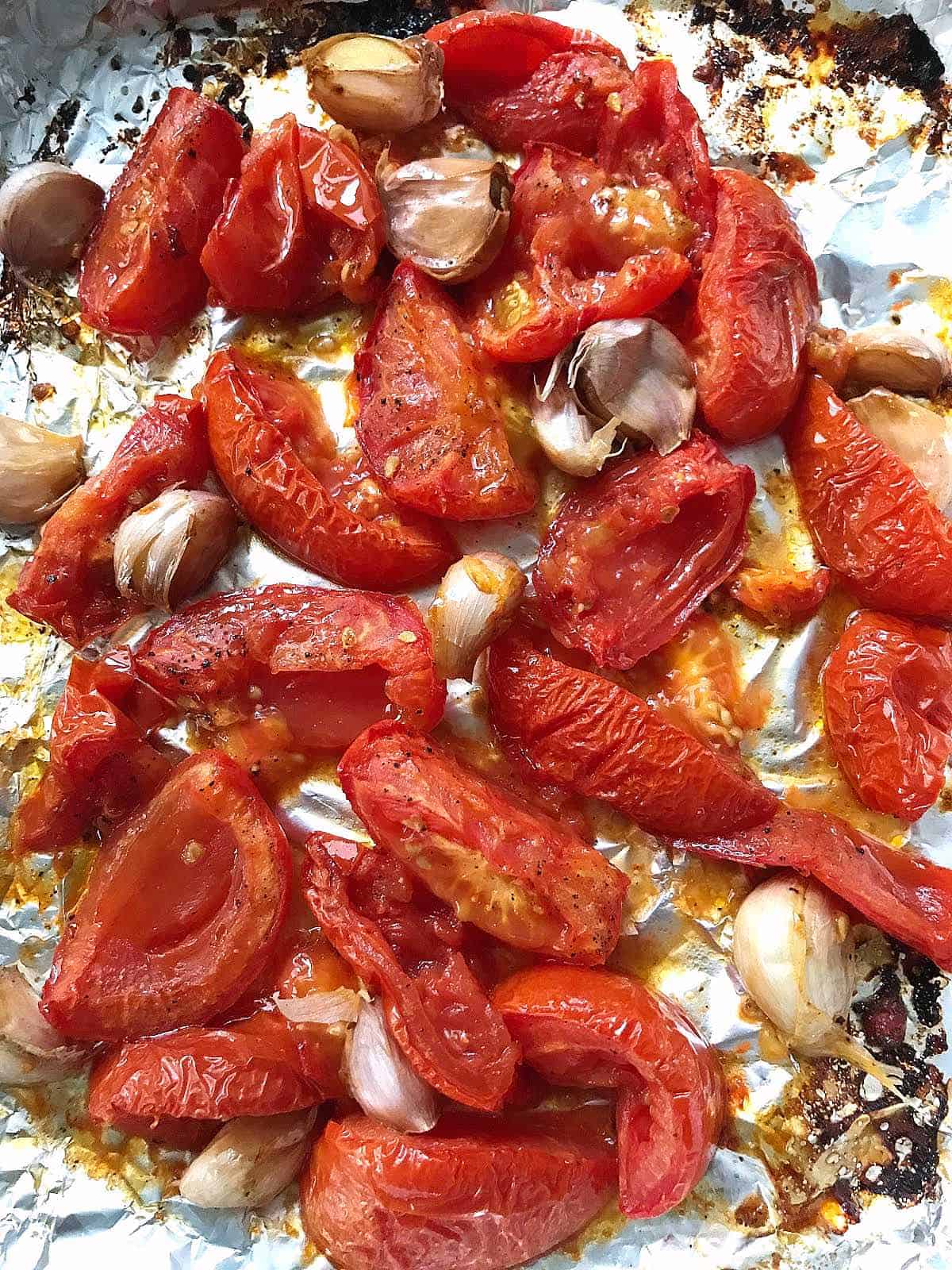 Roasted tomatoes, garlic, and red peppers on aluminum paper.