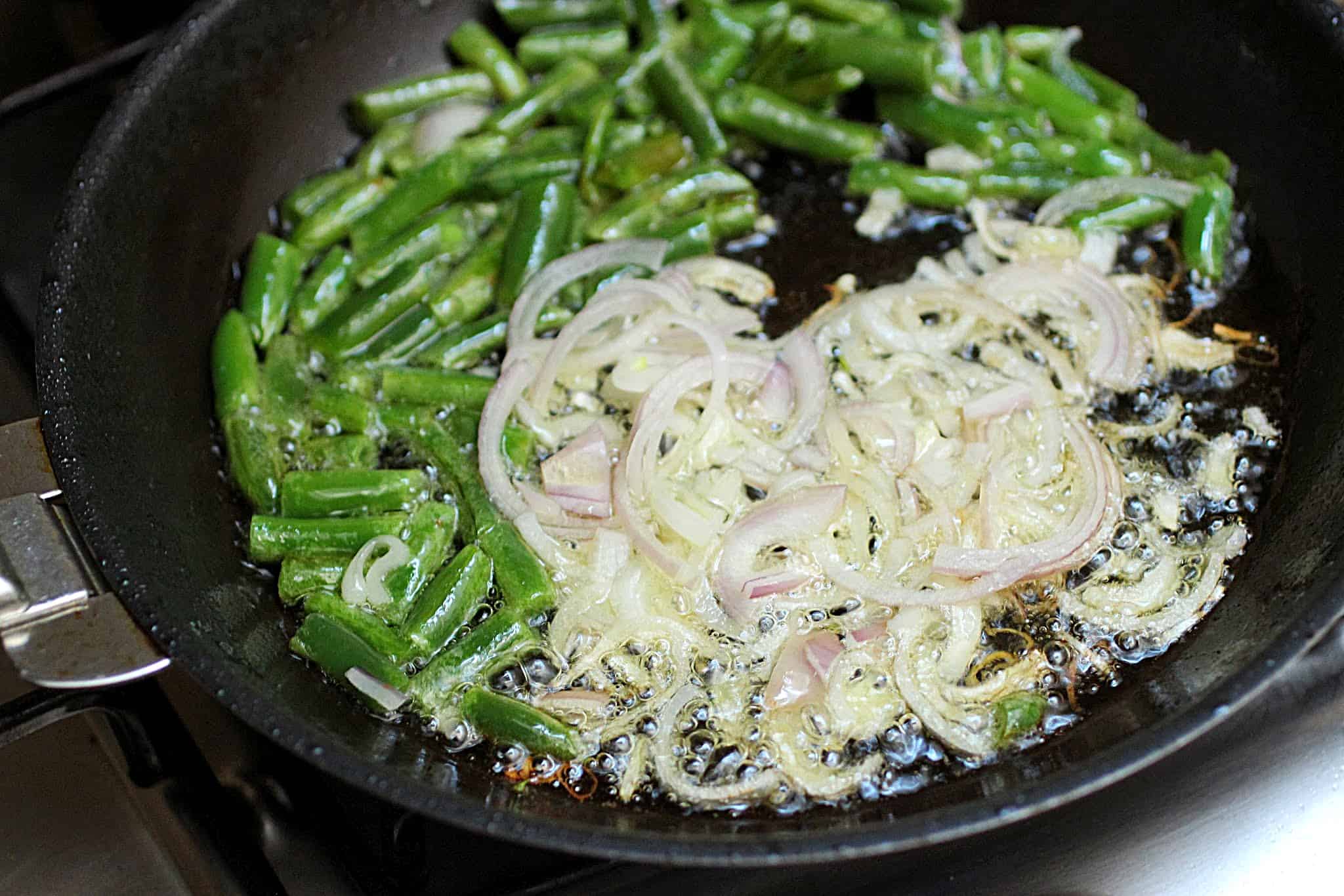 Black skillet with green beans and sliced shallots in oil