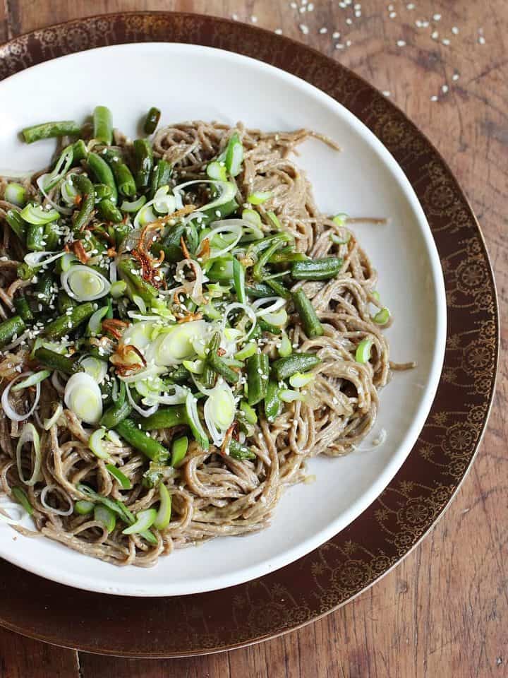 Soba noodle salad topped with green beans on white plate, wooden table