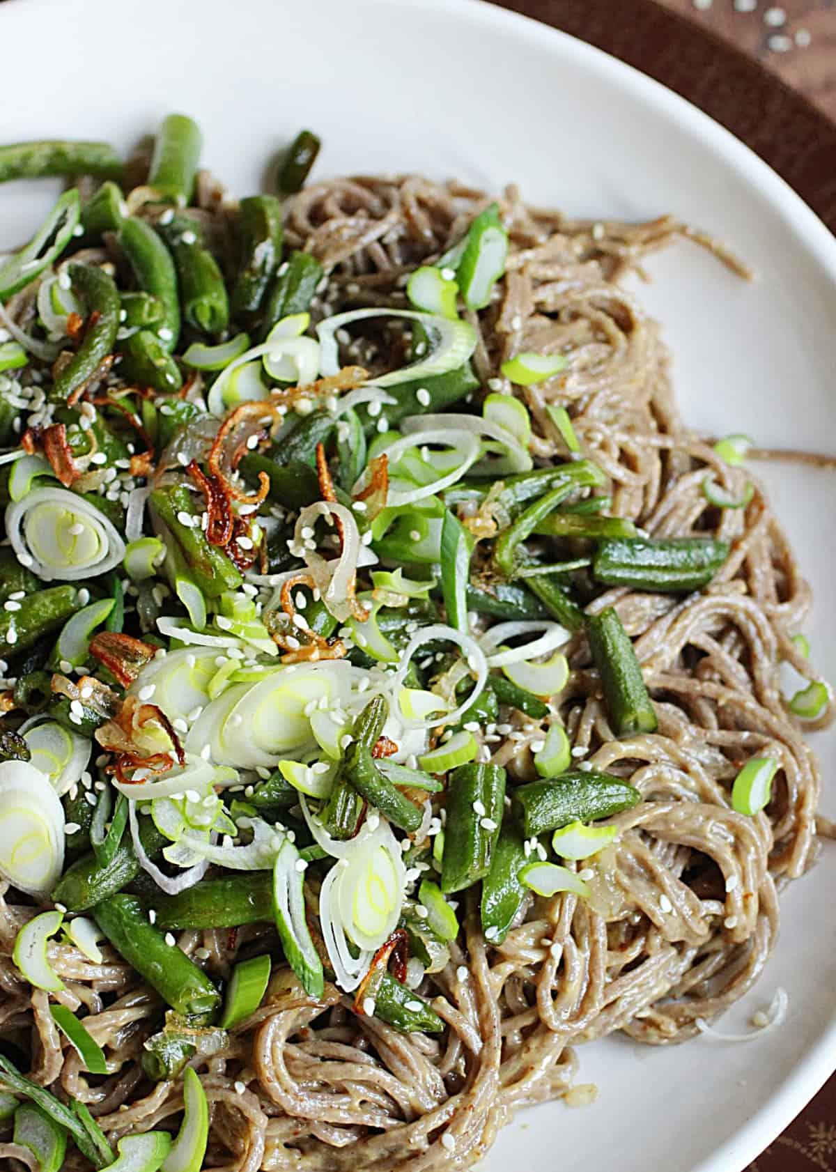 Soba noodle salad with green beans and shallots on white plate, close-up image
