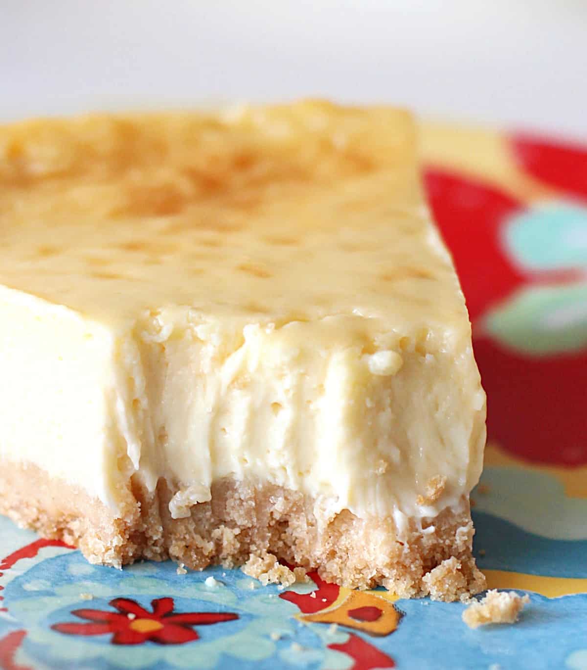 Close up of a colorful plate with a bitten slice of plain cheesecake, crumbs and fork marks