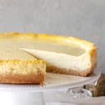Plain cheesecake with missing slice on a white cake stand, greay background