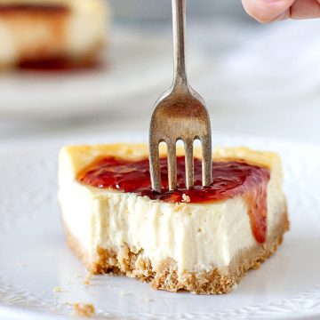 Whitish background and plate with eaten slice of jam covered cheesecake with a silver fork.