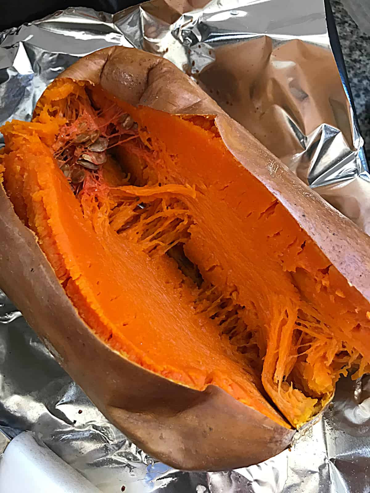 Whole baked butternut squash cut in half on a piece of aluminum paper.