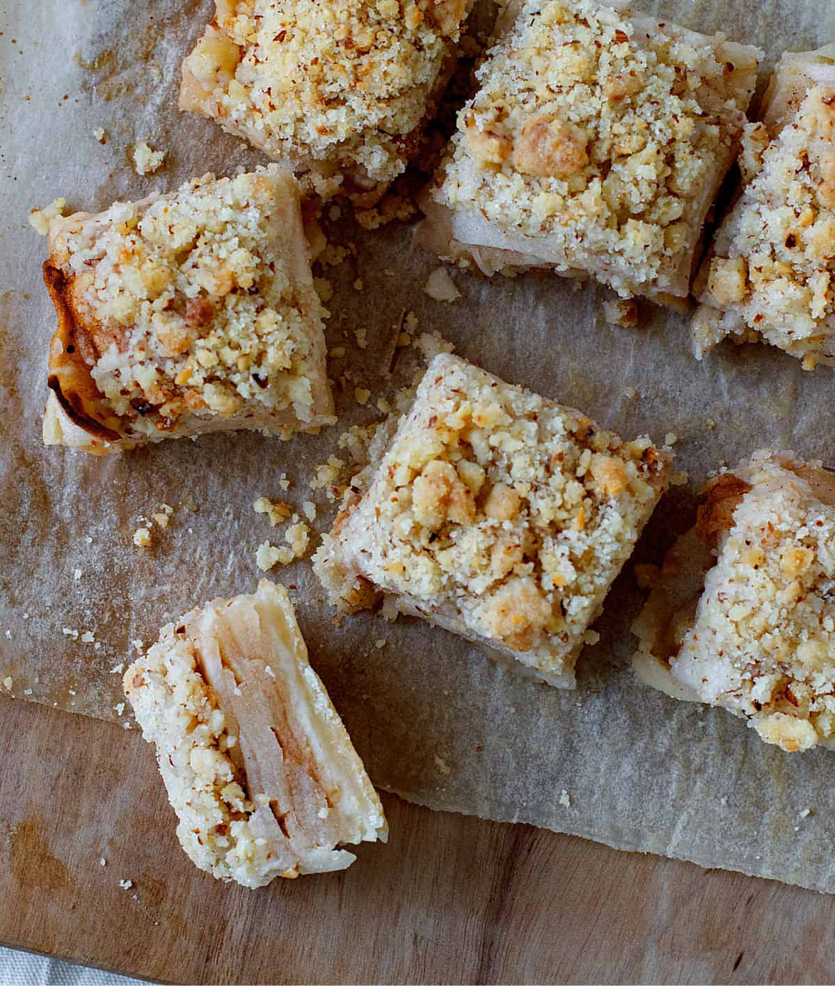 Top view of apple pie crumb bars on light wooden board and parchment paper