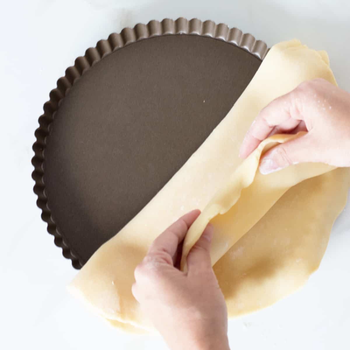 Hands lining metal tart pan with pie crust.