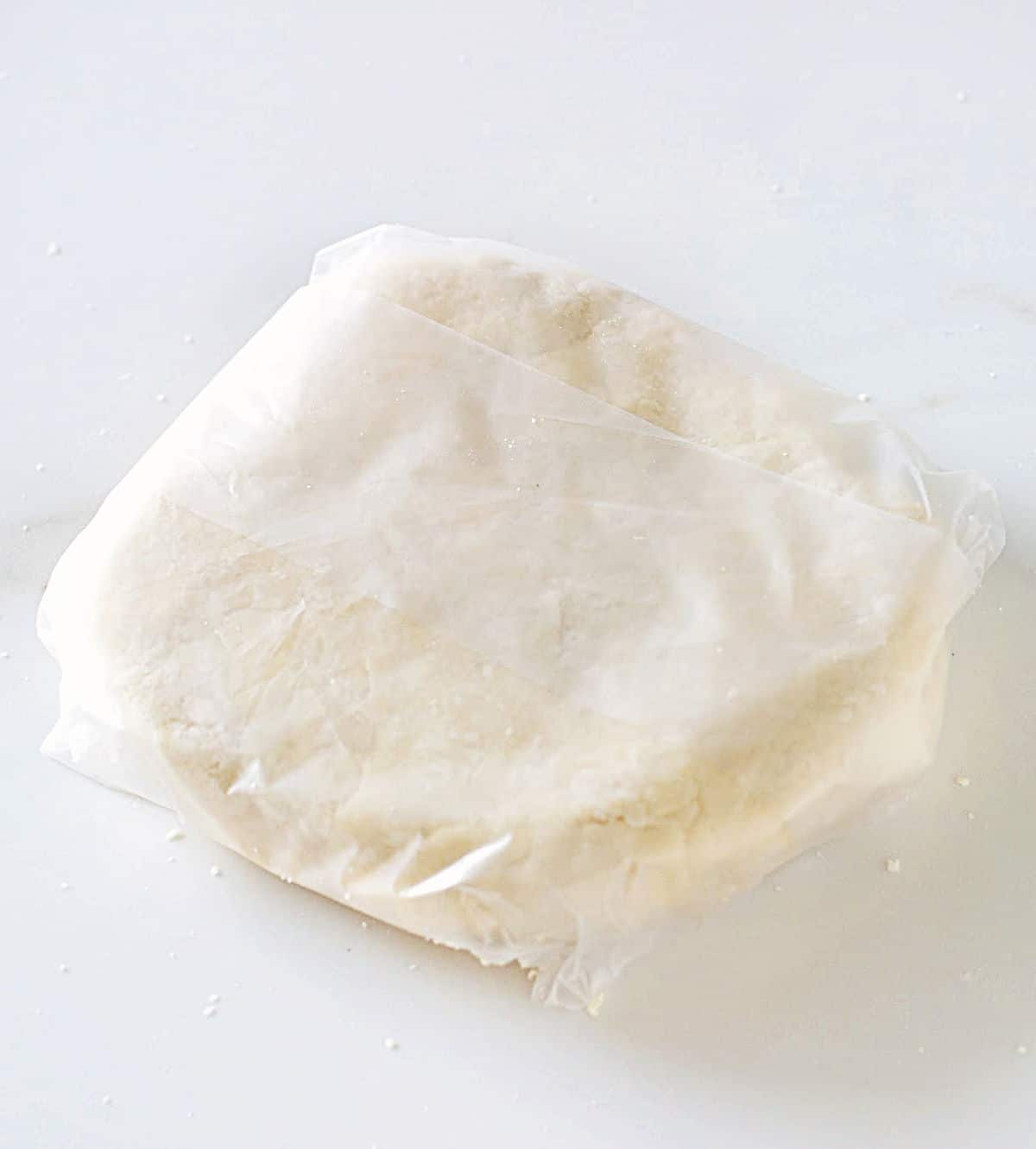 Wrapped disc of pie crust on a white marble surface.