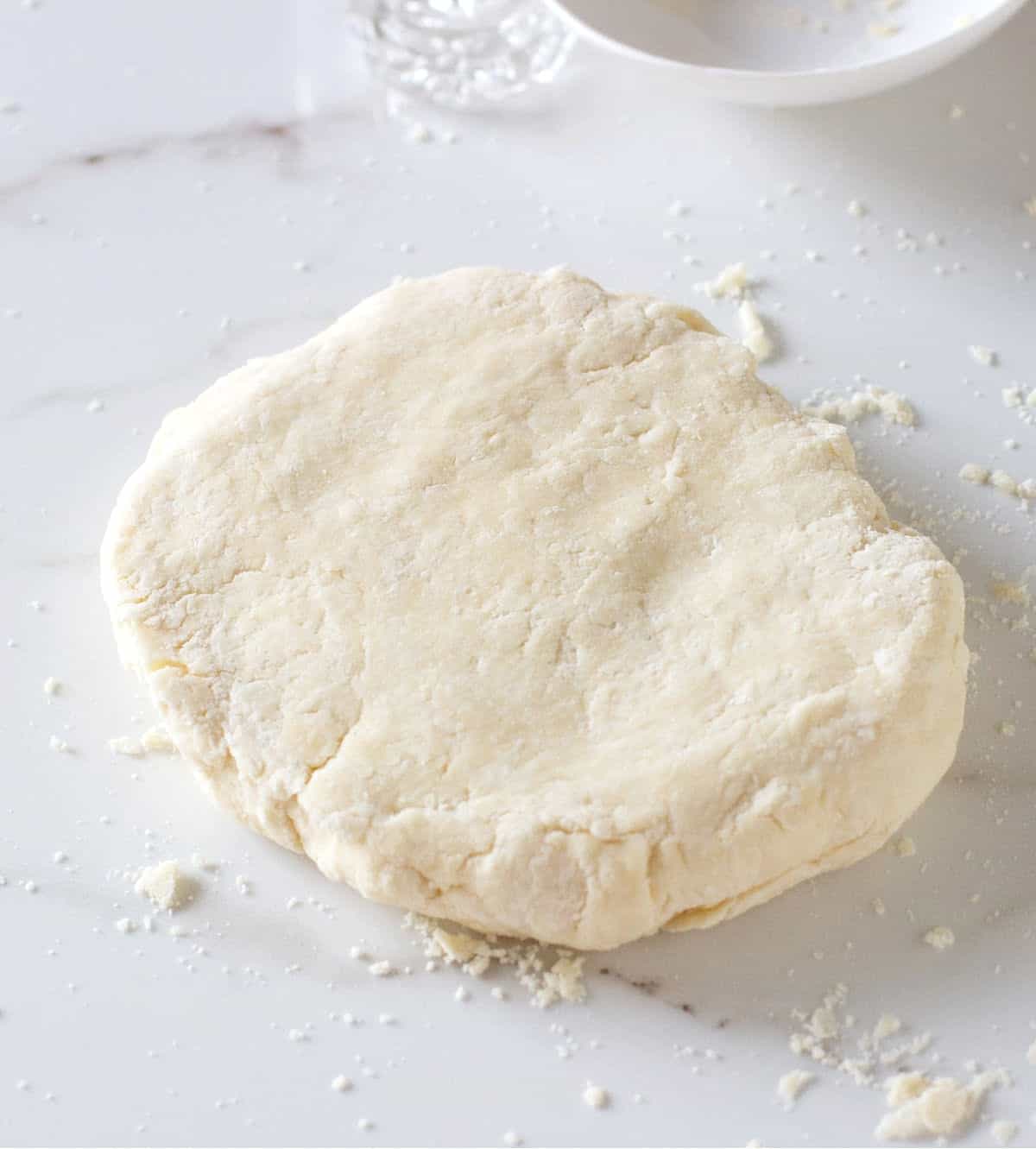 Round piece of pie crust dough on a white marble surface.