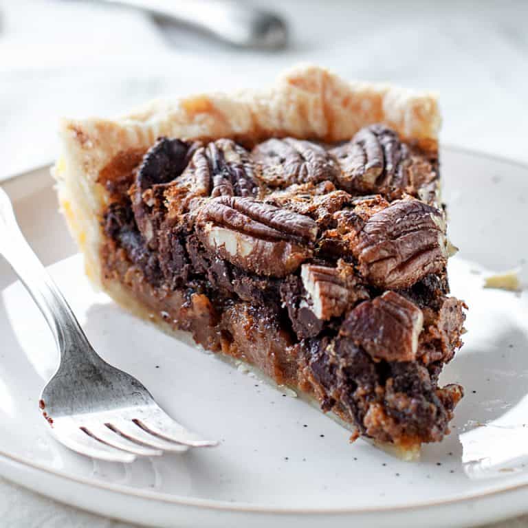 Slice of pecan pie with chocolate on whitish plate, silver fork, white background