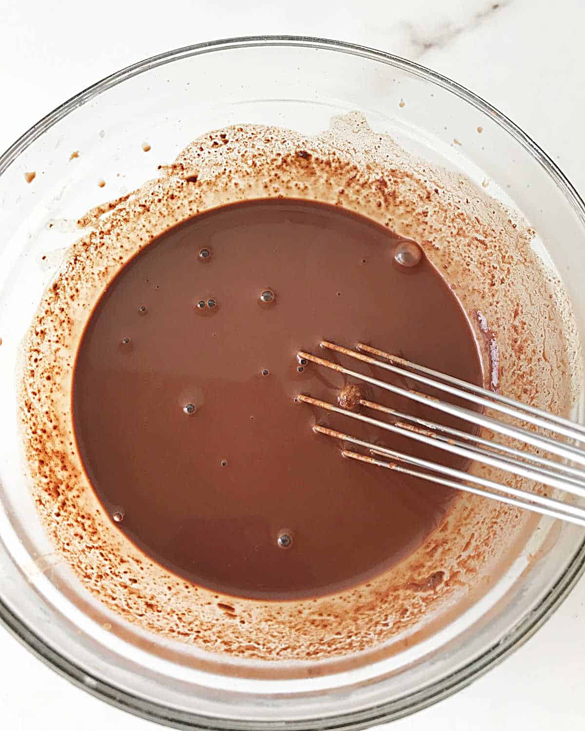 Chocolate custard in a glass bowl with a whisk.