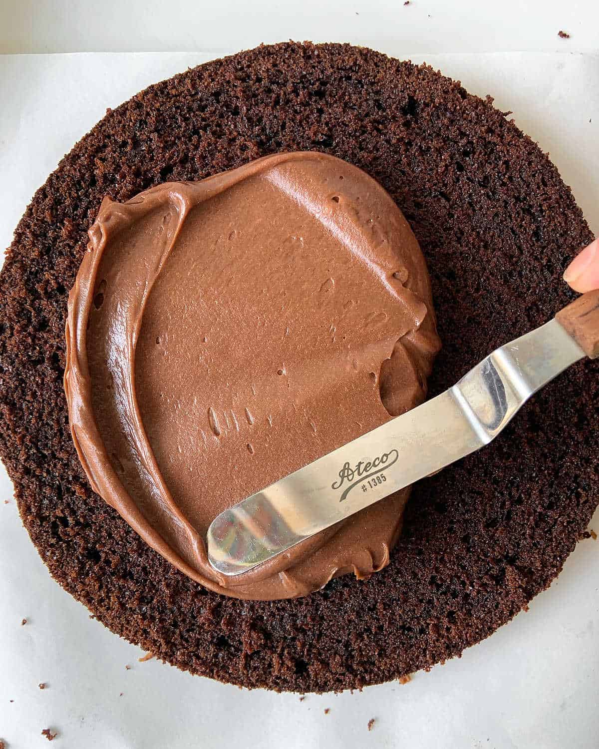 Spreading chocolate filling on a chocolate cake layer with an offset spatula.