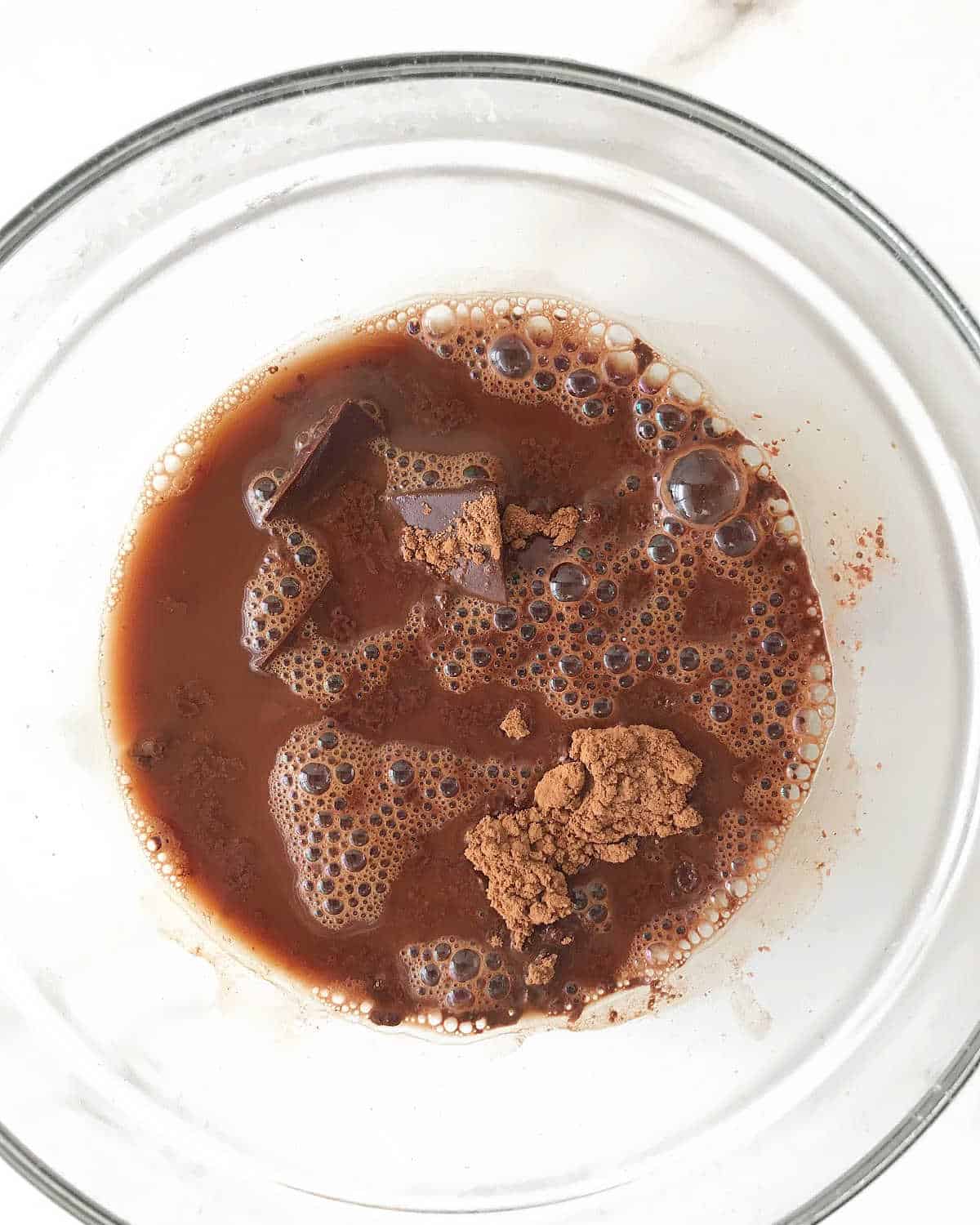 Cocoa powder, chocolate and coffee in a glass bowl on a white surface. 