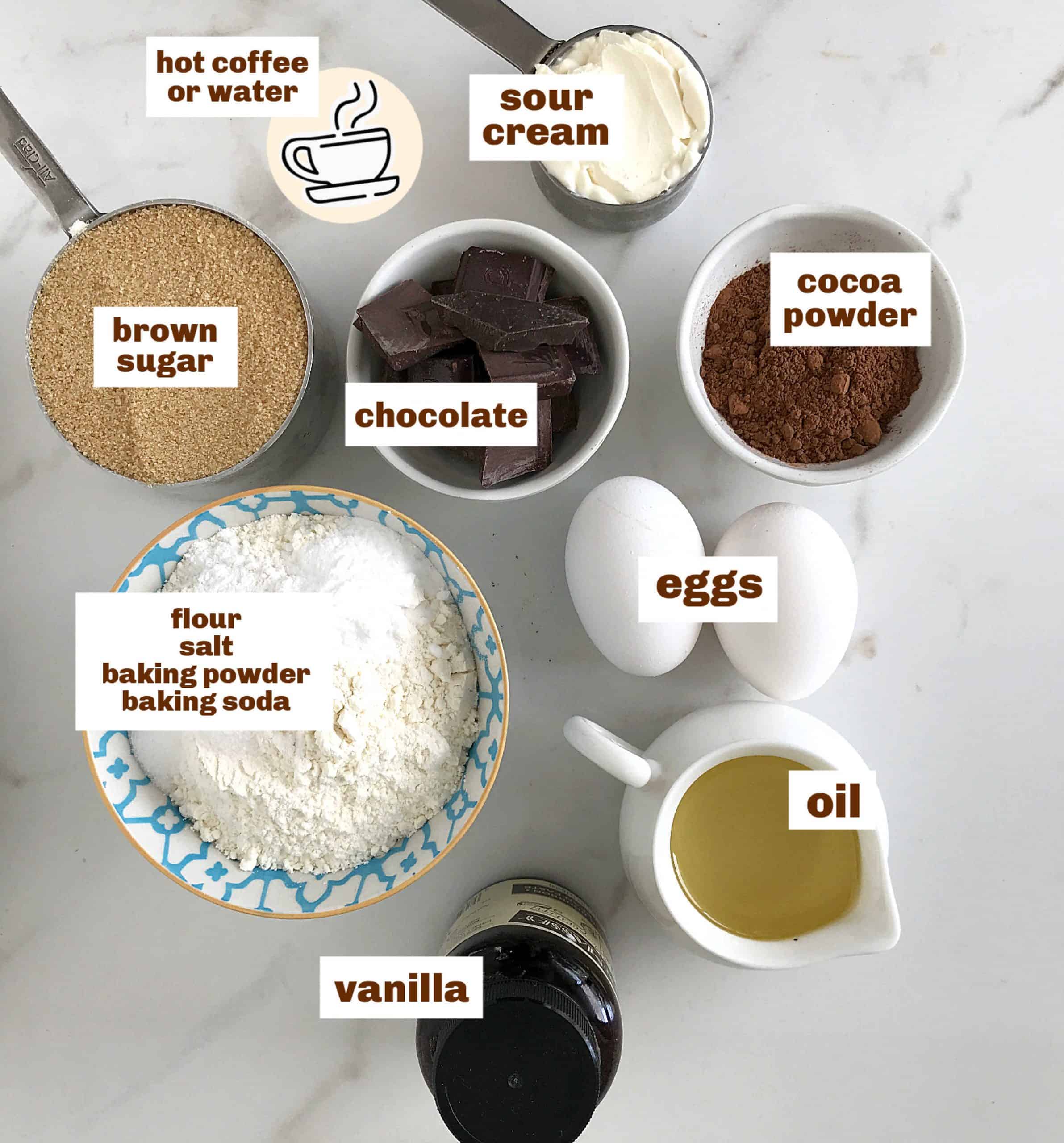 White marble surface with several bowls with ingredients for chocolate layer cake, image with text