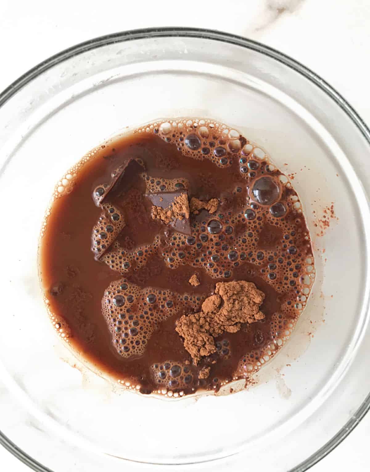 White surface with glass bowl containing chocolate, cocoa powder and water