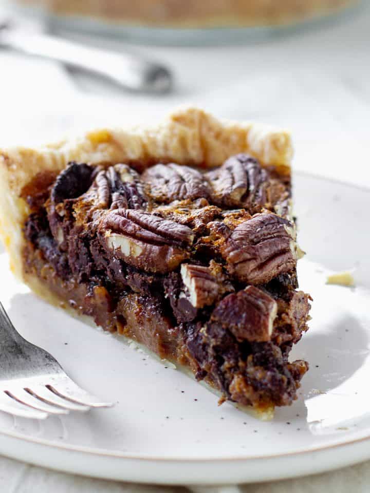 White background and plate with slice of pecan pie, a silver fork