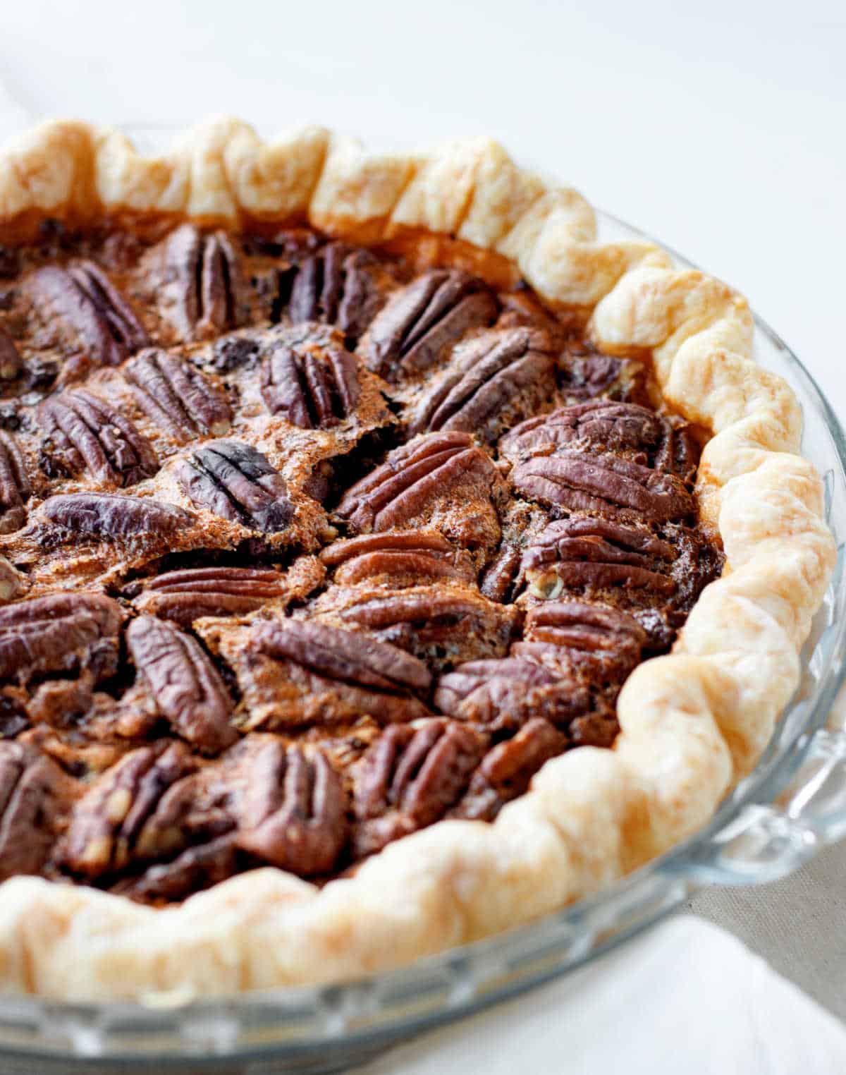 Baked pecan pie in a glass dish on a white surface. Partial view.