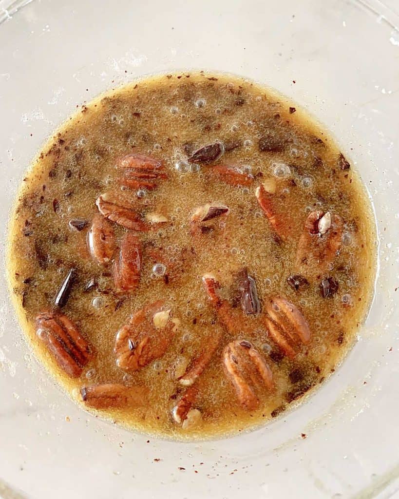 Pecans and chocolate chunks with rest of pecan pie filling in a glass bowl.