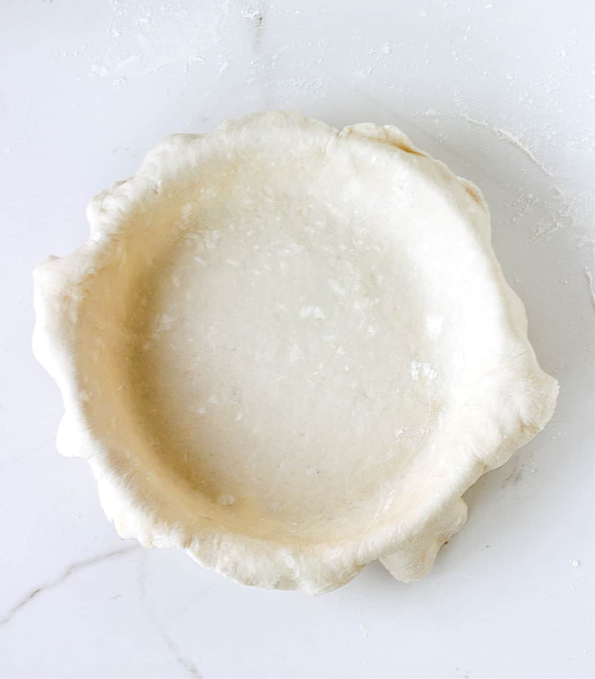 White surface with pie dough overhanging on top of a pie dish