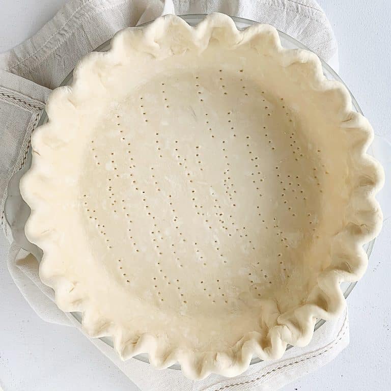 Crimped round unbaked pie crust on a kitchen towel on white surface