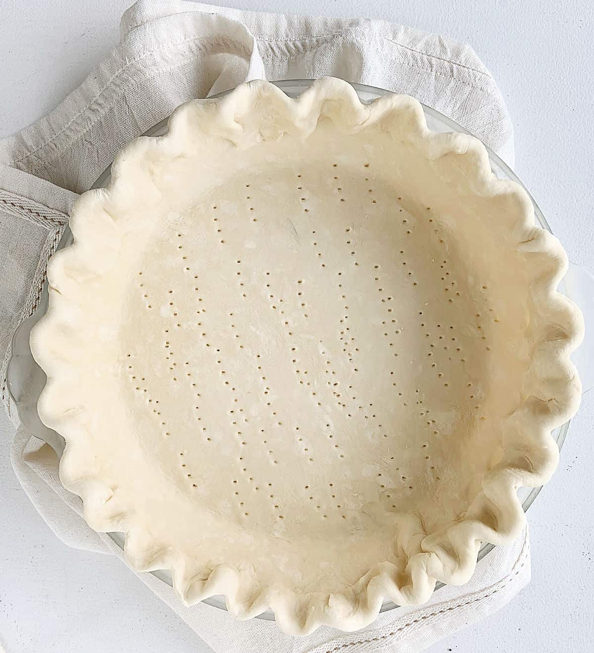 Unbaked whole pie shell with crimpled edges on a light beige cloth on a white table