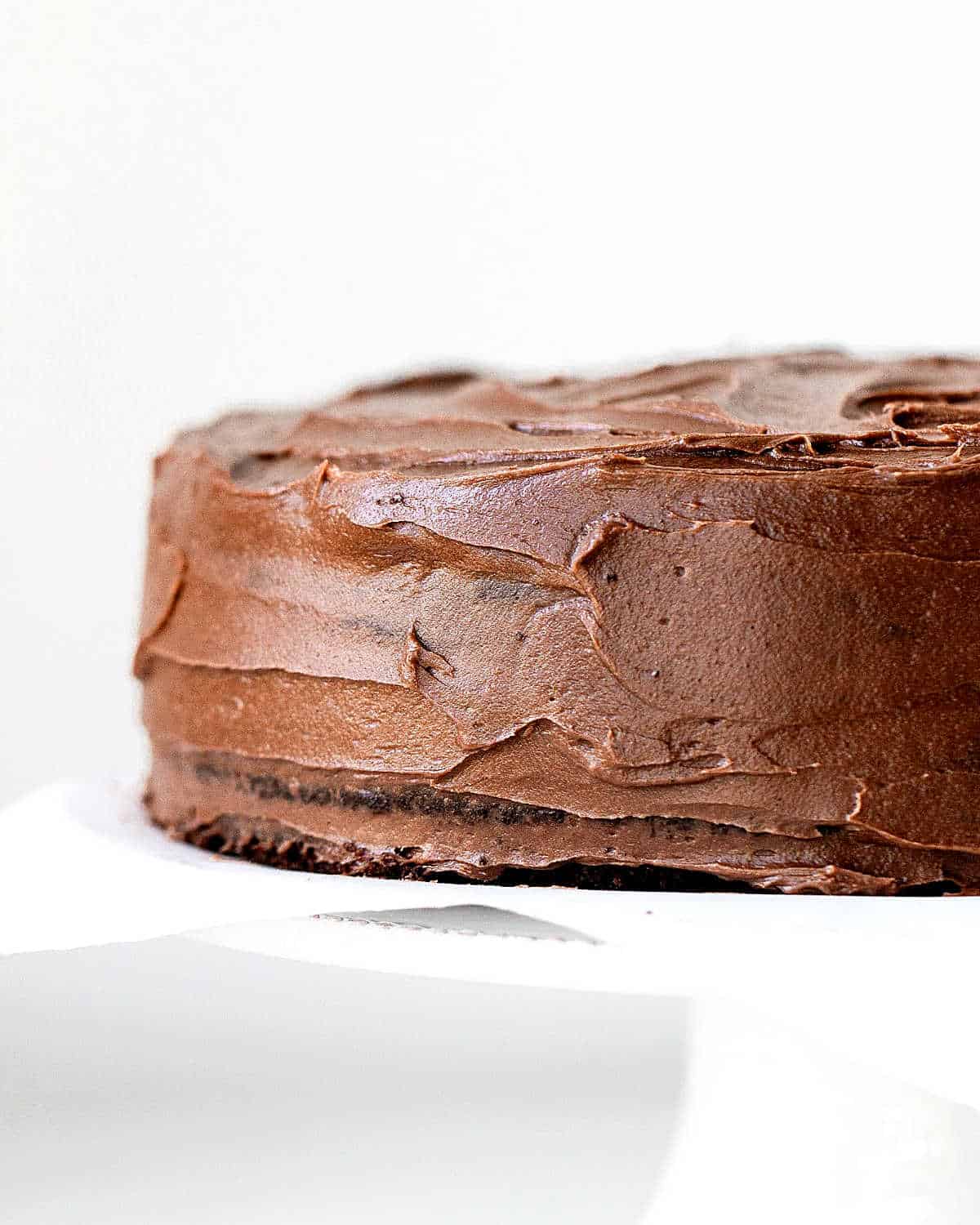 Partial view of frosted chocolate cake on a white cake stand with a white background.