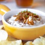 Yellow shallow dish with caramelized onion dip, potato chips around