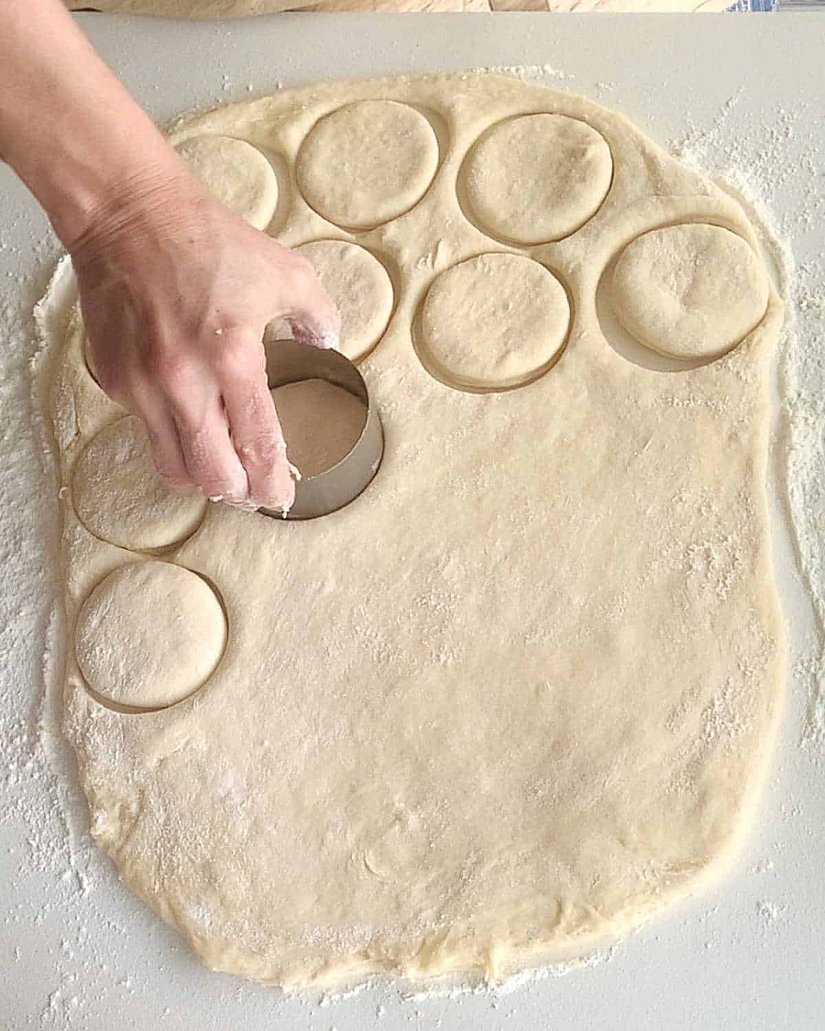 Rolled bread dough and hand cutting rounds with a cookie cutter.