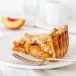 Slice of peach crumb pie on white plate, white backgournd
