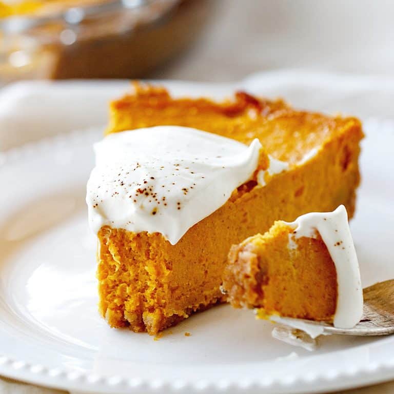 White plate with bitten slice of pumpkin pie, fork with bite beside it