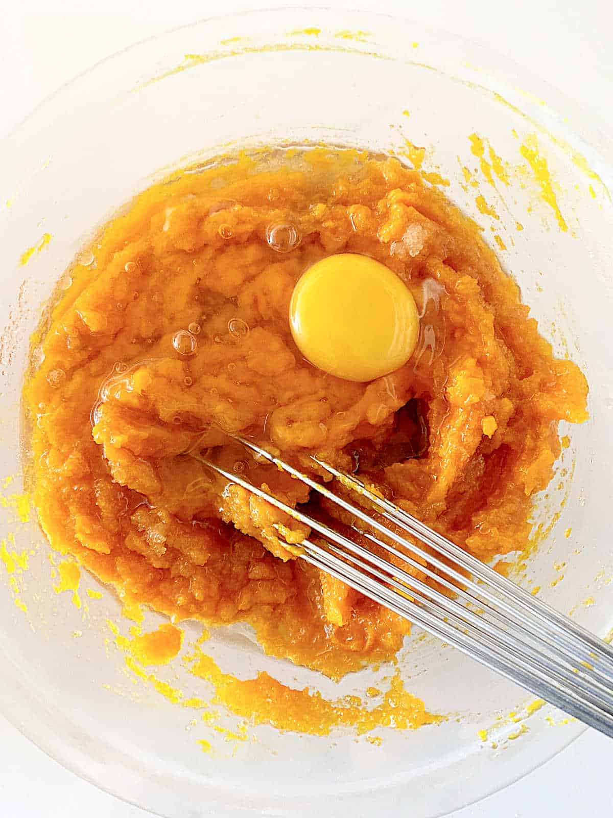 Pumpkin batter with raw egg in a glass bowl with a whisk.