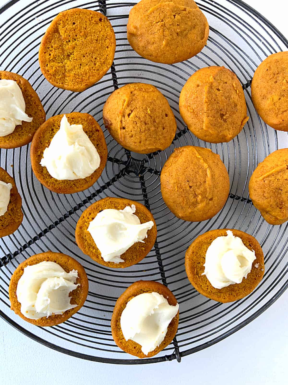 Several pumpkin whoopie pie cookies on a wire rack, some with filling, some plain.