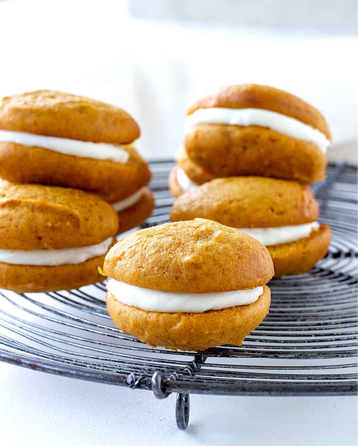 One pumpkin whoopie pie in focus and several others blurred on a round wire rack.