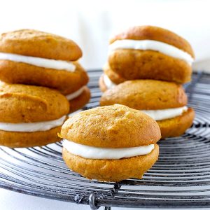 On a metal wire rack, several pumpkin whoopie pies, greyish background