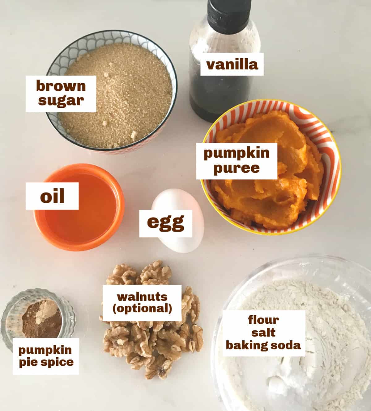Different colored and sized bowls with pumpkin bread ingredients, white surface